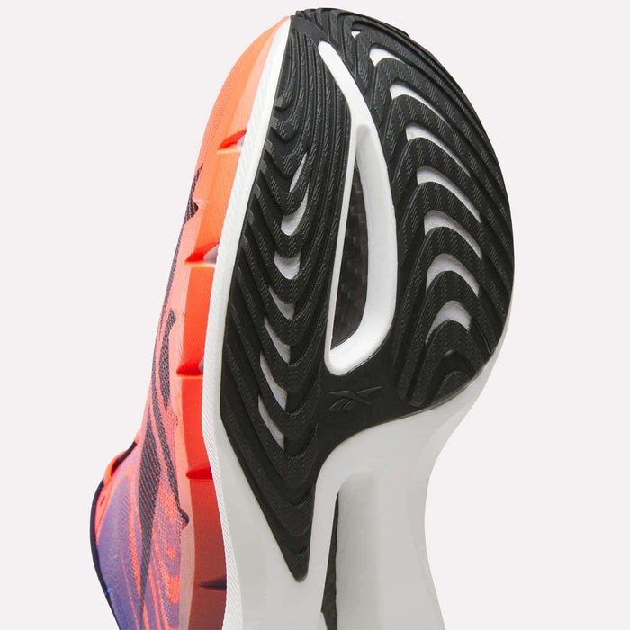Close-up of the sole of a Reebok SpeedShifter Running Shoe, featuring a black and white tread pattern and an orange-pink gradient upper. The shoe is tilted to highlight its textured bottom, innovative HyperFloat foam cushioning, and distinctive side design.