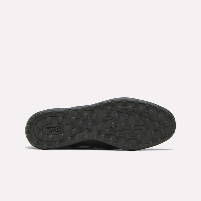 The image displays the black rubber sole of the Reebok Strike Turf Soccer Shoes, viewed from below. The sole features round traction bumps ideal for turf soccer play and practice, along with an abstract Reebok logo near the heel.