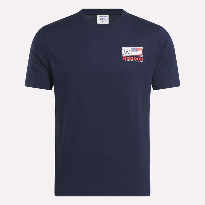 The Reebok USA Football T-Shirt is a navy blue, short-sleeve cotton jersey with a left chest patch featuring a soccer ball, American flag, red Reebok logo, and "International" text.