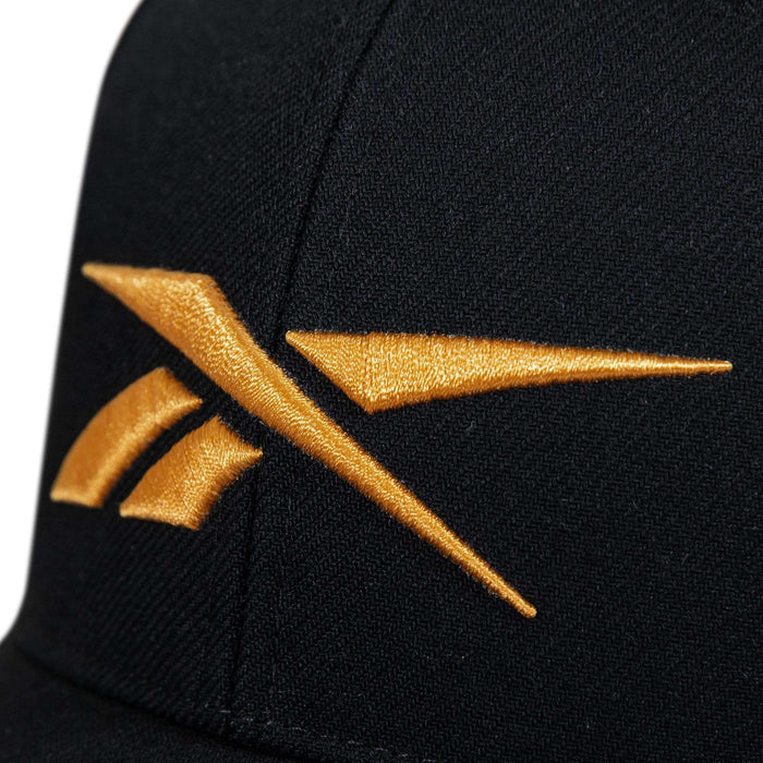 Close-up of the Reebok Vector Baseball Cap in black fabric, showcasing an embroidered golden Reebok logo on the front.