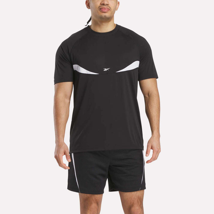 A man stands facing forward against a plain white background, wearing a black Reebok Warm-Up Basketball T-Shirt with white accents and matching black training shorts.