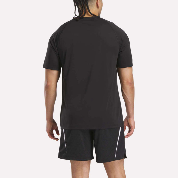 A man with braided hair is shown from the back, wearing a black Reebok Warm-Up Basketball T-Shirt and black shorts with white side stripes, standing against a plain white background.
