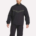 A person wearing the Reebok Warm Up Track Jacket in black with a gray chest stripe and matching black pants, standing against a plain light background.