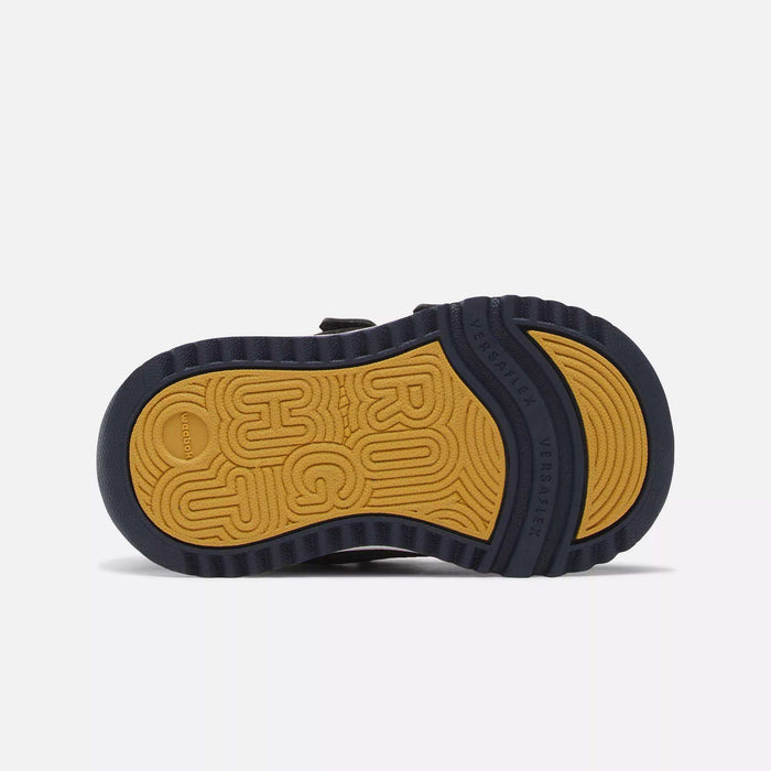 The image shows the sole of the Reebok Weebok Clasp Low Shoes for infants and toddlers, with a tan and black design. “ROUGH” is embossed on the tan section, Versartex appears near the heel, and ridged black edges provide grip.