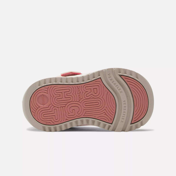 The image shows the sole of a Reebok Weebok Storm X Shoes - Infant & Toddler, featuring a textured pink and beige pattern. The pink center has bold raised letters, and "Versaflex" is labeled on the beige outer edge.