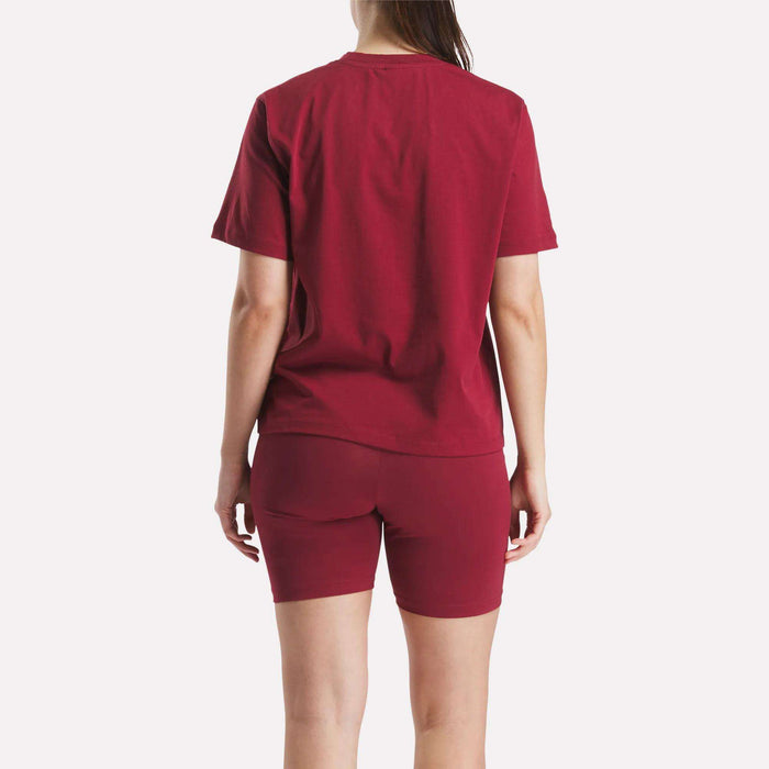 A person faces away from the camera, wearing a matching Reebok Women's Big Logo Oversized Crew Short Sleeve Tee and maroon shorts. The scene is set against a plain white background.