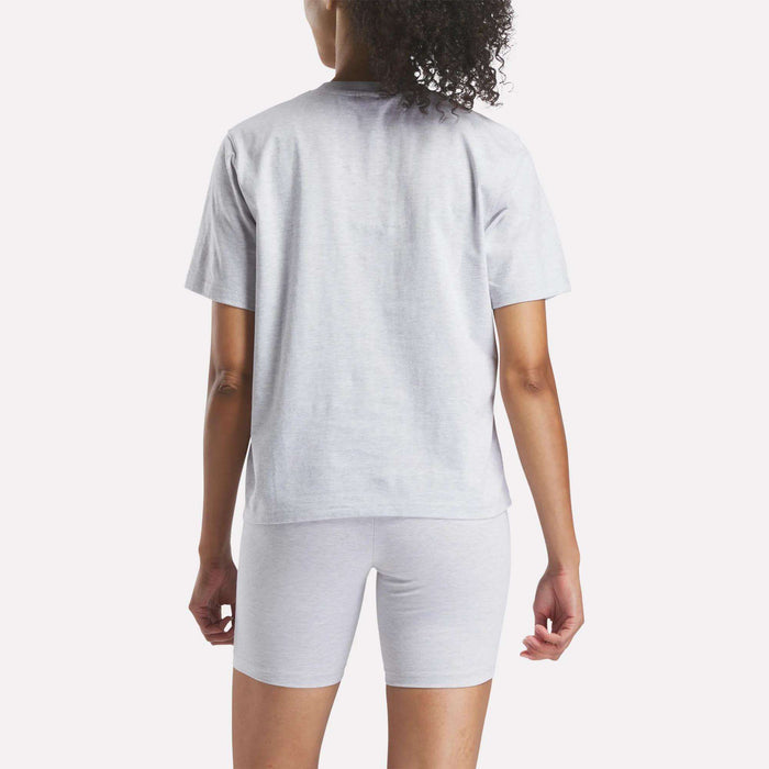 A person with curly hair is seen from behind wearing a light gray Reebok Women's Big Logo Oversized Crew Short Sleeve Tee against a plain white background.