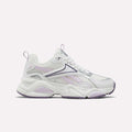 Reebok Women’s Charge Shoes in White/Purple feature a chunky sole, cushioned midsole, breathable mesh upper, and lace-up closure. Shown against a plain light background, these versatile athletic sneakers are perfect for training.