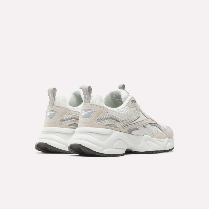 A pair of Reebok Women’s Charge Shoes in light beige and white, featuring gray accents, the Reebok logo on the heel, chunky white soles, and black tread, positioned on a plain white background and angled slightly to the left.