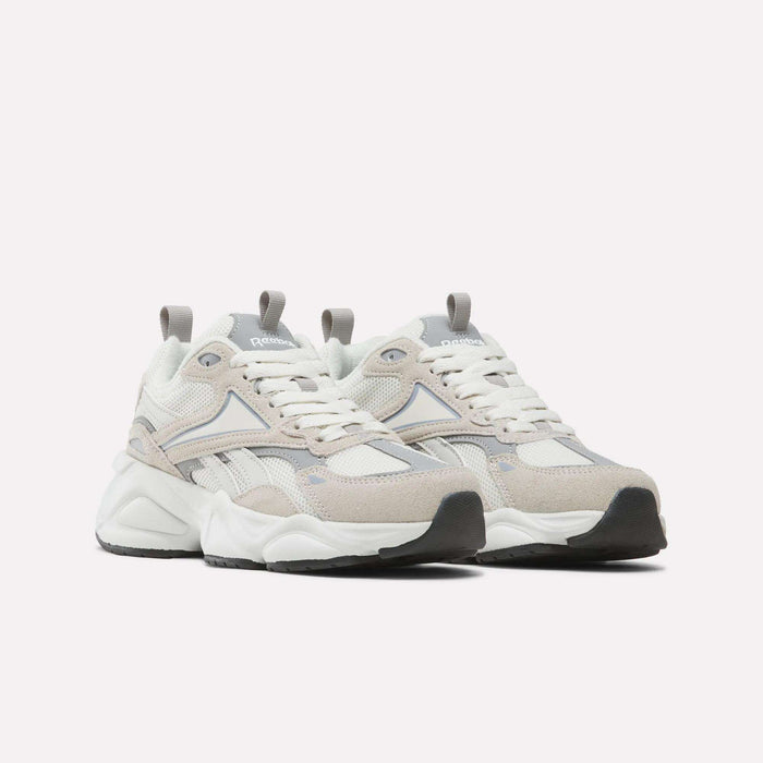 A pair of Women’s Charge Shoes by Reebok, featuring beige, white, and gray tones with chunky soles, mesh panels, and suede accents, is displayed against a plain white background. These athletic shoes for women seamlessly combine style and comfort for everyday wear.
