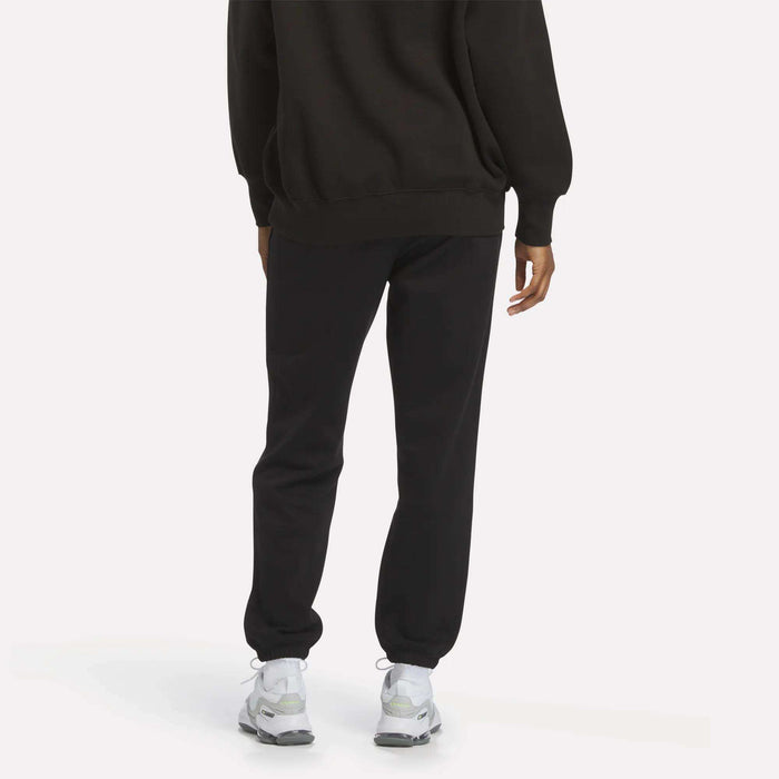 A person is seen from behind wearing Reebok Women’s Cinch Sweatpants with a modern design, paired with a black sweatshirt and white sneakers, set against a plain light background.