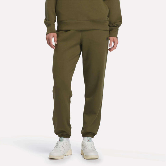 A person wearing Reebok Women’s Cinched Joggers in Olive Stone, a matching sweatshirt, and white sneakers stands against a plain white background.