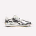 A pair of Reebok Women’s Classic AZ Shoes in Silver/Chalk/Gum, featuring a metallic silver upper with white laces and cream accents, are displayed against a plain light background.