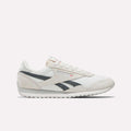 Side view of Reebok Women's Classic AZ Shoes in white with light gray suede accents, black stripes, flat rubber sole, plus Reebok logo and small Union Jack on the side.