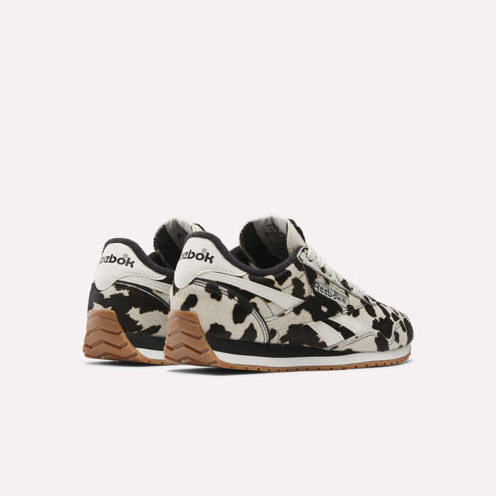 Reebok Women's Classic AZ Shoes feature a bold black and white cow print, brown gum soles, and Reebok logos on the heels and sides. Displayed on a white background, these sneakers add standout style to any outfit.