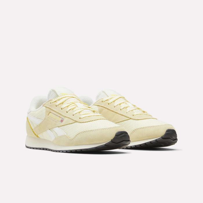 A pair of Reebok Women’s Classic AZ Shoes in beige and white with yellow accents, featuring a crochet textile upper, white laces, and black soles, are displayed on a plain white background.