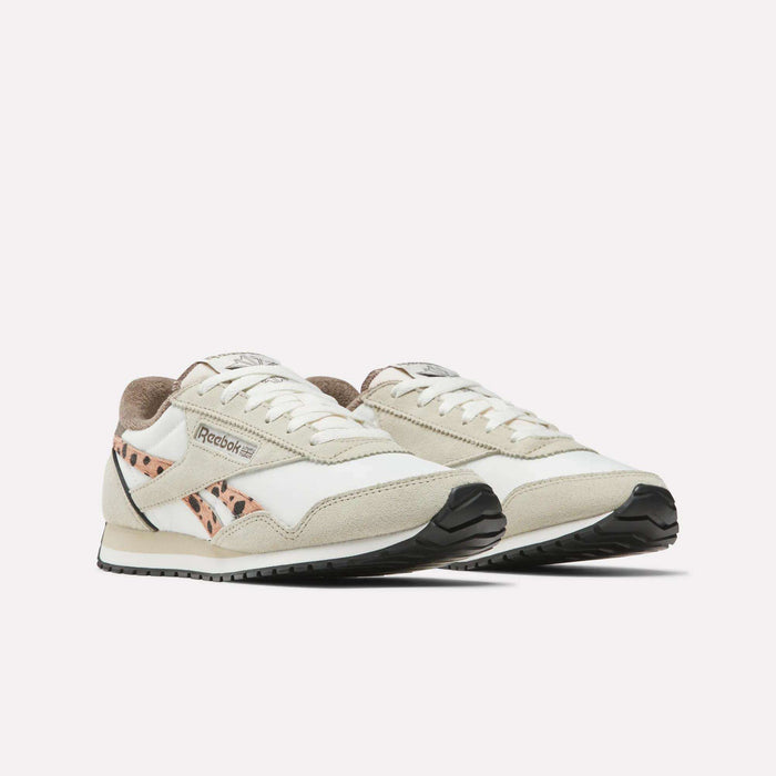 The Reebok Women's Classic AZ Shoes feature a white and beige design with black soles and animal-print accents, blending retro style with modern flair. Displayed on a plain white background.