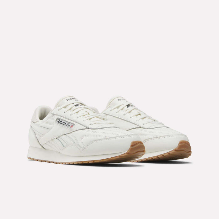 A pair of Reebok Women's Classic AZ Shoes in white with gum soles, shown at an angle. These shoes feature a leather upper, white laces, refined stitching details, and display the Reebok logo on both the side and tongue.