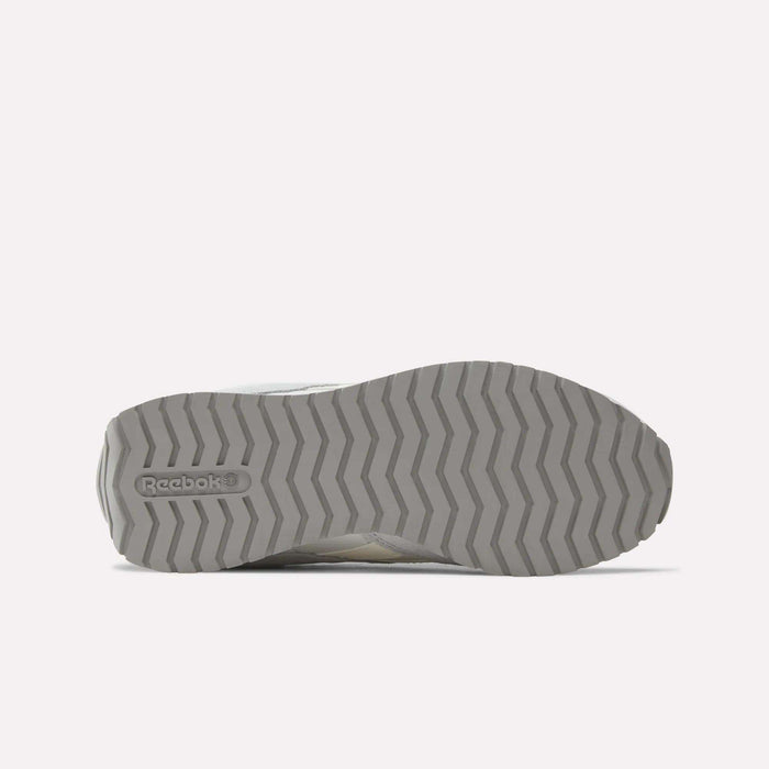 The image shows the gray rubber sole of the Reebok Women's Classic AZ Shoes with a zigzag tread and embossed logo on the left, emphasizing their low-profile design. The background is plain and light-colored.