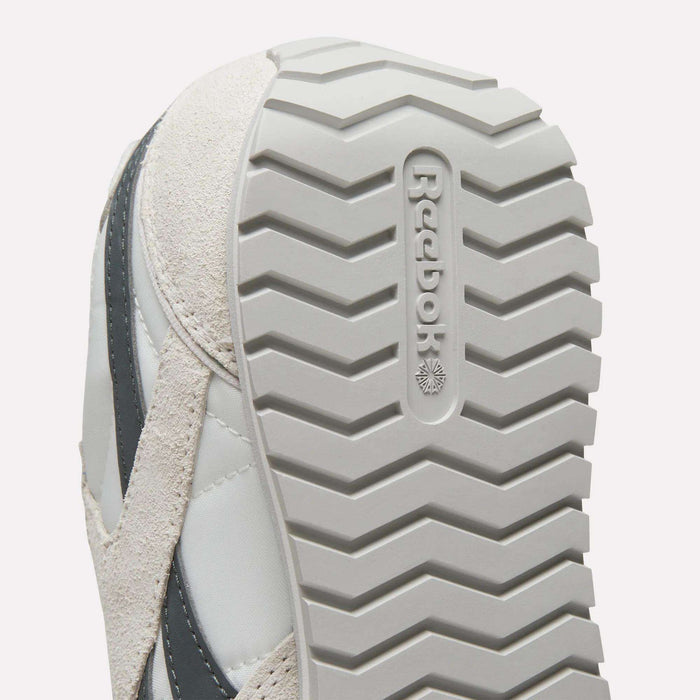 Close-up of the sole on Women's Classic AZ Shoes by Reebok, highlighting the zigzag tread and embossed Reebok logo. These vintage sneakers come in light gray and beige.