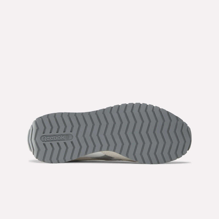 The image shows the gray rubber outsole of Reebok Women's Classic AZ Shoes with a zigzag tread and embossed logo, set against a light gray background that highlights these vintage style sneakers.