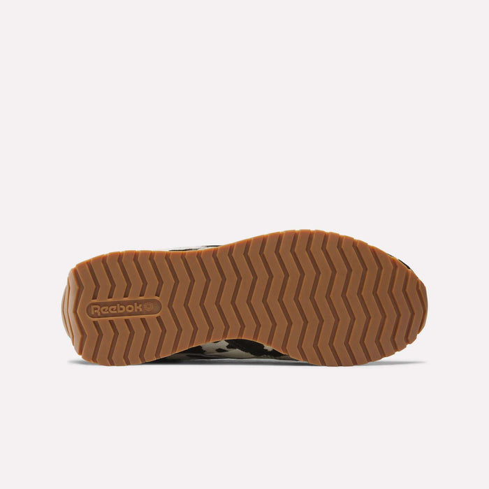 The image shows the bottom of the Reebok Women's Classic AZ Shoes with a tan, zigzag-patterned rubber sole and the embossed Reebok logo near the heel, highlighting their stylish design.