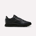 The Reebok Women's Classic Leather Shoes are shown in side profile against a white background, featuring black leather, cushioned midsole, black laces and sole, and the white and red Reebok logo on the side and heel.