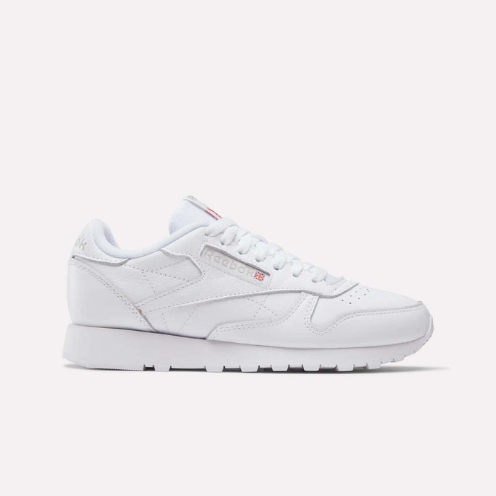 The Women's Classic Leather Shoes by Reebok feature white laces, a low-cut design, minimal stitching, a cushioned midsole, and the iconic Reebok logo with British flag on the side. The sole is also white.