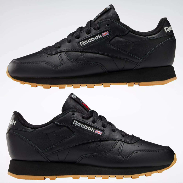 A side view of Reebok Women's Classic Leather Shoes in black with gum soles; visible features include cushioned midsoles, Reebok logos, and a small UK flag on the side and heel.