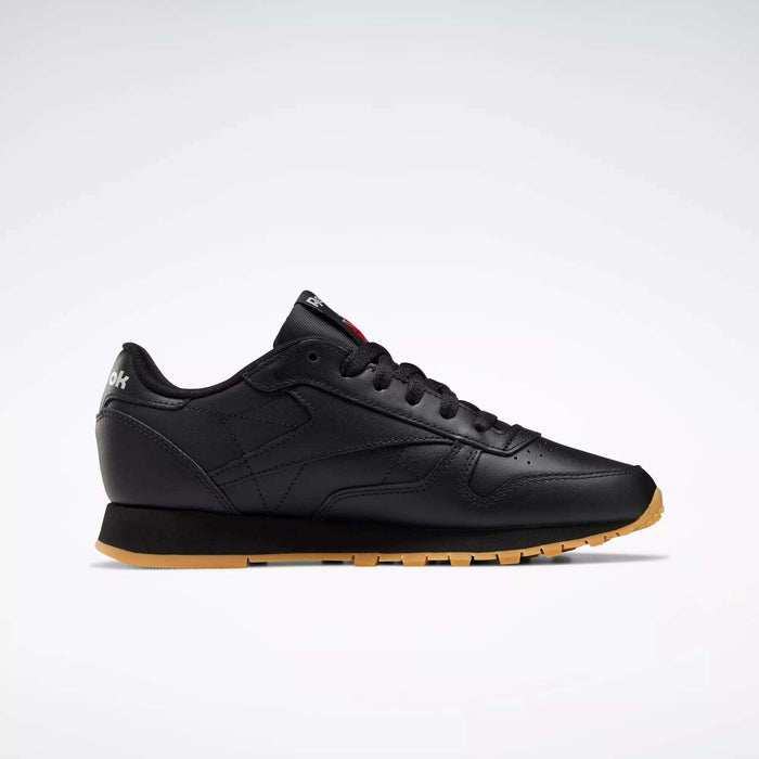 The Reebok Women's Classic Leather Shoes are shown in side profile with a black leather upper, gum sole, black laces, subtle stitching, and a cushioned midsole for comfort, set against a plain white background.