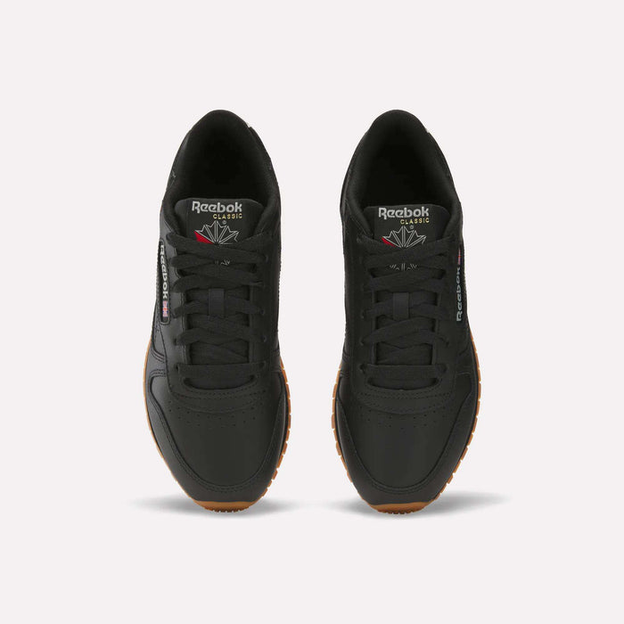 A pair of Women's Classic Leather Shoes by Reebok in black with gum soles, shown from above. They display the Reebok logo on the tongue and side, feature cushioned midsoles, and have neatly tied laces for comfort and style.
