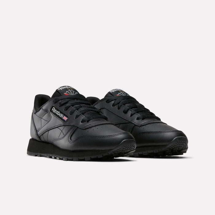 A pair of Women's Classic Leather Shoes by Reebok in black, featuring black laces, a cushioned midsole, and visible Reebok logo with British flag on the side and tongue, displayed against a plain light background.
