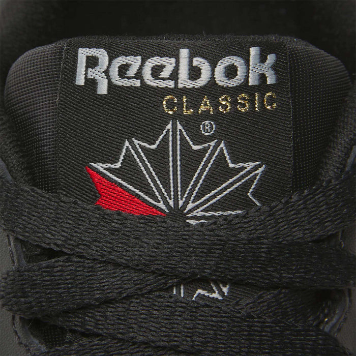 Close-up of a Women's Reebok Classic Leather Shoe tongue, showing the white Reebok logo and CLASSIC in gold above a stylized maple leaf, with black laces in front and a cushioned midsole for comfort.