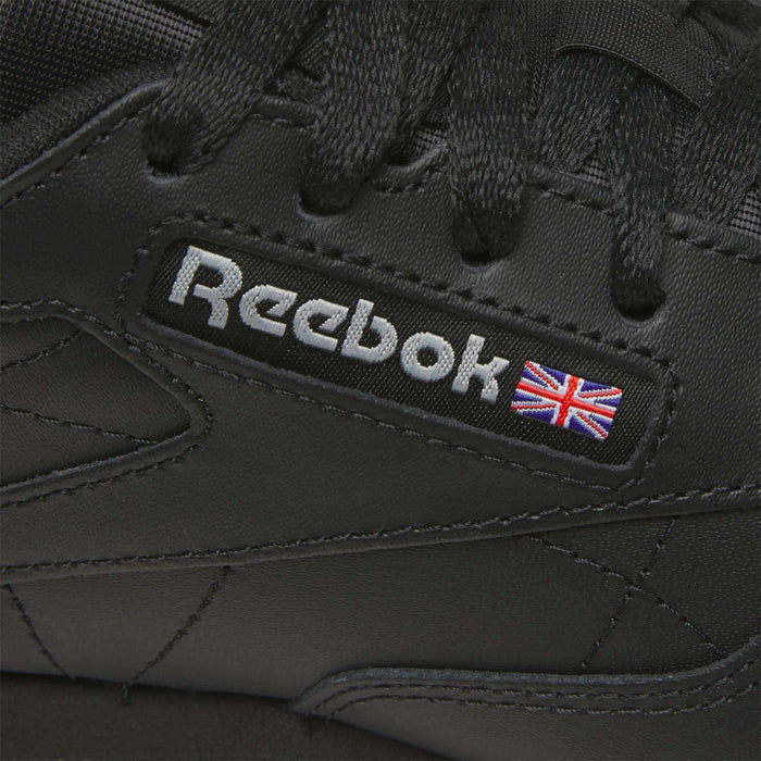 Close-up of Reebok Women's Classic Leather Shoes in black, showcasing the Reebok logo, a small Union Jack flag by the laces, and a cushioned midsole for comfort.