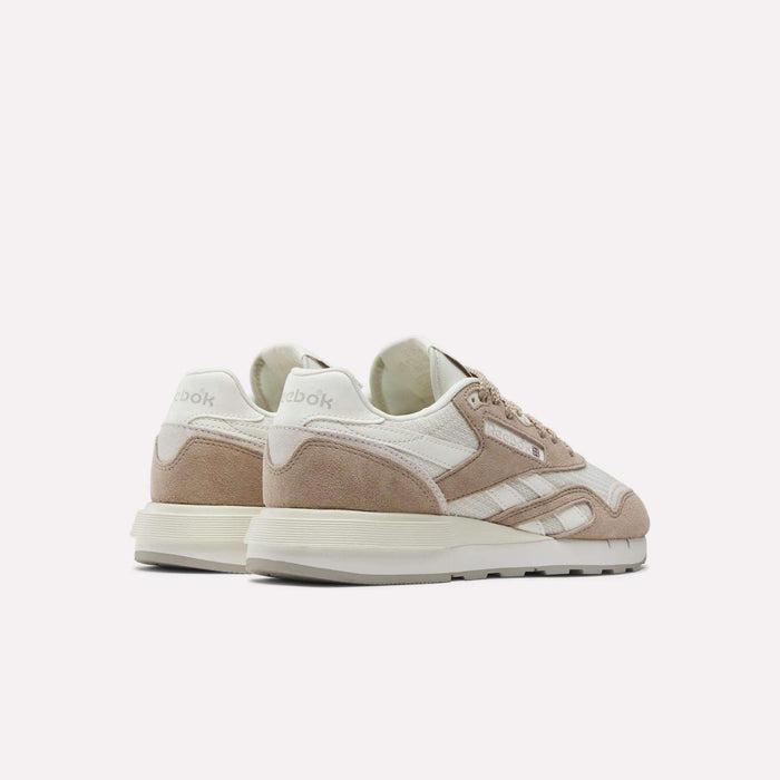 The Women’s Classic Nylon 89 Shoes by Reebok, shown in beige and white suede and mesh with white midsoles, feature a retro running style and heel branding, viewed from the back and angled to the side.