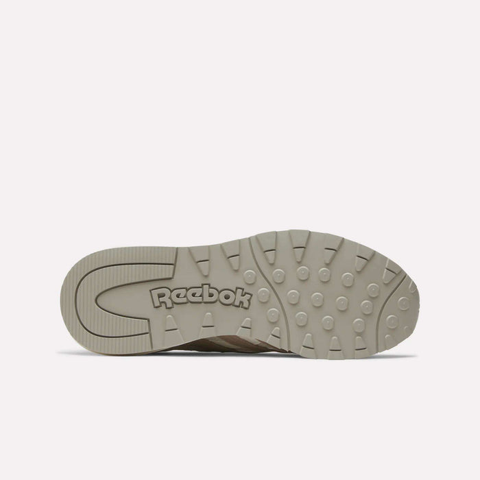 The image shows the beige rubber sole of the Reebok Women's Classic Nylon 89 Shoes, viewed from underneath. Circular grip patterns and an embossed Reebok logo near the heel highlight its retro design.