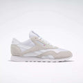 The Reebok Women's Classic Nylon Shoes are shown in a side profile, featuring white with beige suede accents, white laces, and a white sole against a light background—versatile sneakers for everyday style.