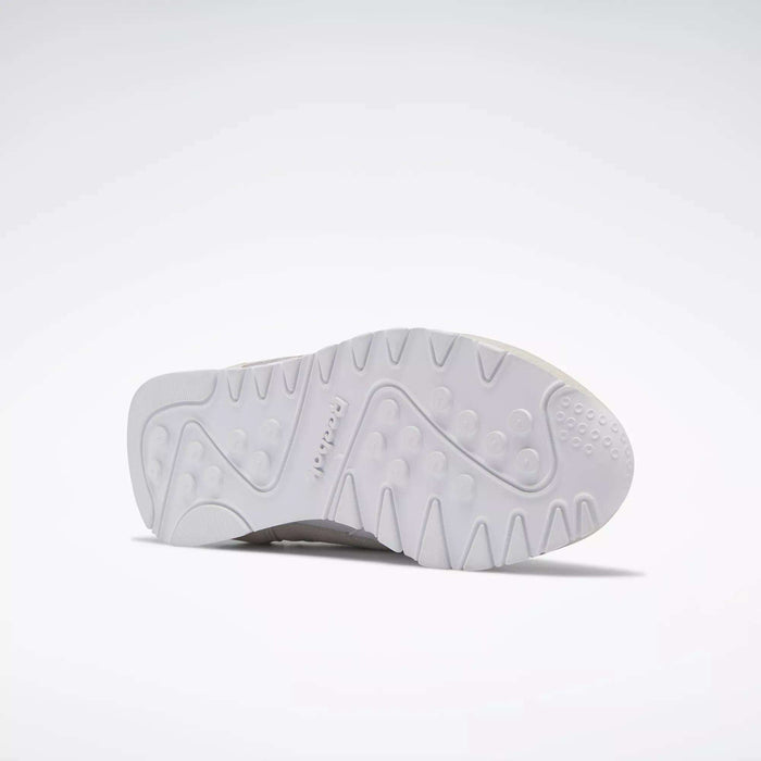 The image shows the white rubber sole of Reebok Women's Classic Nylon Shoes, viewed from below with a textured pattern and circular grooves. The Reebok logo is embossed near the center, emphasizing these versatile everyday sneakers.