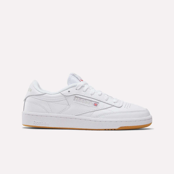 The Reebok Women's Club C 85 Shoes feature a white low-cut design, perforated toe, white laces, subtle branding, and a light brown rubber sole; shown on a plain white background.