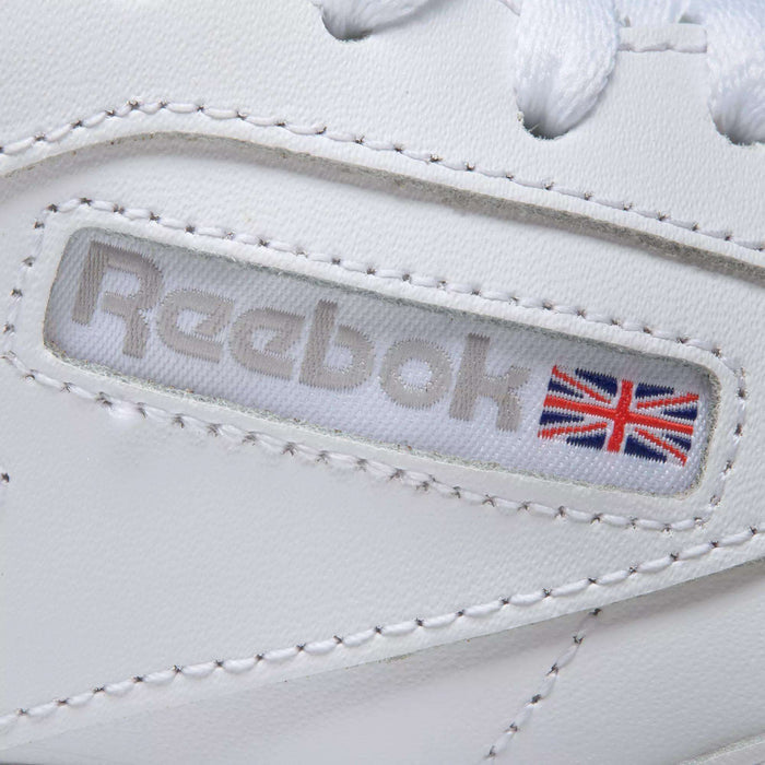 Close-up of Reebok Women's Club C 85 Shoes in white, highlighting the Reebok logo and a small Union Jack flag on the side, detailed stitching, and part of the white shoelaces at the top.
