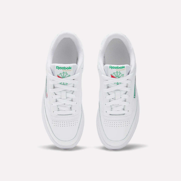 The Women's Club C 85 Shoes by Reebok are white sneakers with green Reebok logos and tongue detailing, a clean minimalist look, and toe perforations, shown from an overhead view.