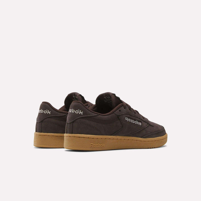 A pair of dark brown Reebok Women's Club C 85 Shoes with gum soles, viewed from the back and side, featuring the Reebok logo on both the heel and side.