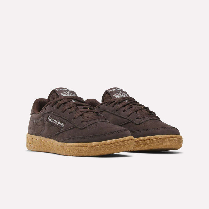 Reebok Women's Club C 85 Shoes in dark brown with gum soles, featuring Reebok logos on the side and tongue, are classic leather sneakers shown on a plain white background—timeless style from Reebok.