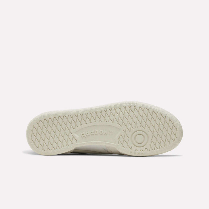 The image displays the beige rubber sole of the Women’s Club C 85 Shoes by Reebok, viewed from the bottom. It features a herringbone tread pattern and a circular design near the front, with the Reebok logo embossed in the center. This classic style is commonly seen in nubuck leather footwear and is a staple in popular women’s tennis shoe collections.