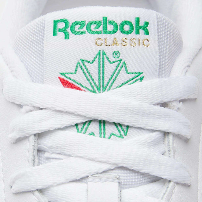 Close-up of Women's Club C 85 Shoes by Reebok, featuring a white design, green Reebok logo on the tongue, gold “CLASSIC” text, a red and green star detail, and crisp white laces—an iconic choice for women.