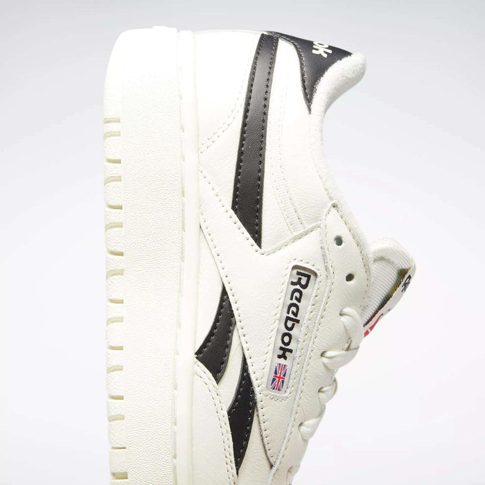 The Reebok Women's Club C Double Revenge Shoes are white with black accents, a thick textured double outsole, and a side logo with a Union Jack flag for classic court-inspired style.
