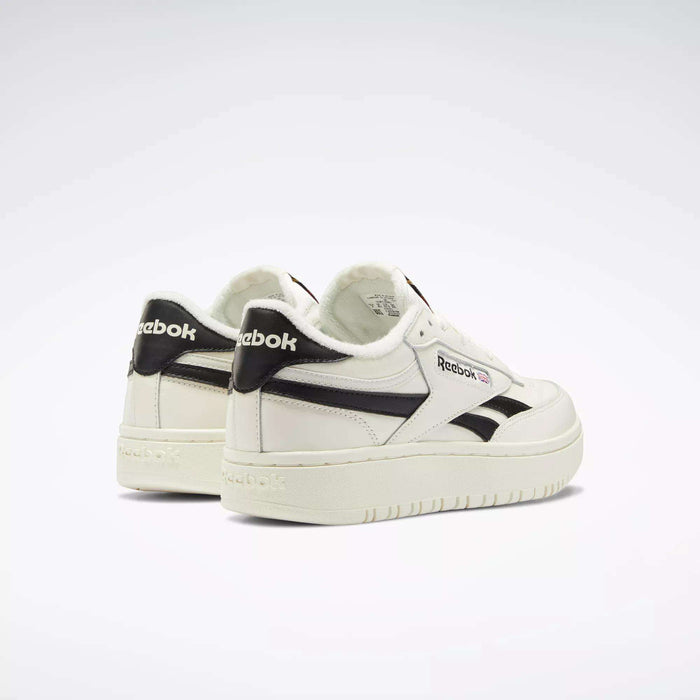 A pair of Reebok Women's Club C Double Revenge Shoes, featuring black accents and logo with a double outsole for style, are arranged side by side on a light background. The left shoe turns outward, highlighting the Reebok heel branding.