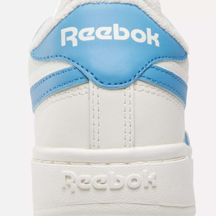 Close-up of the back of a white Reebok Women’s Club C Double Revenge shoe with light blue accents, featuring the Reebok logo in white on both the heel tab and back of the leather upper. Court-inspired design.
