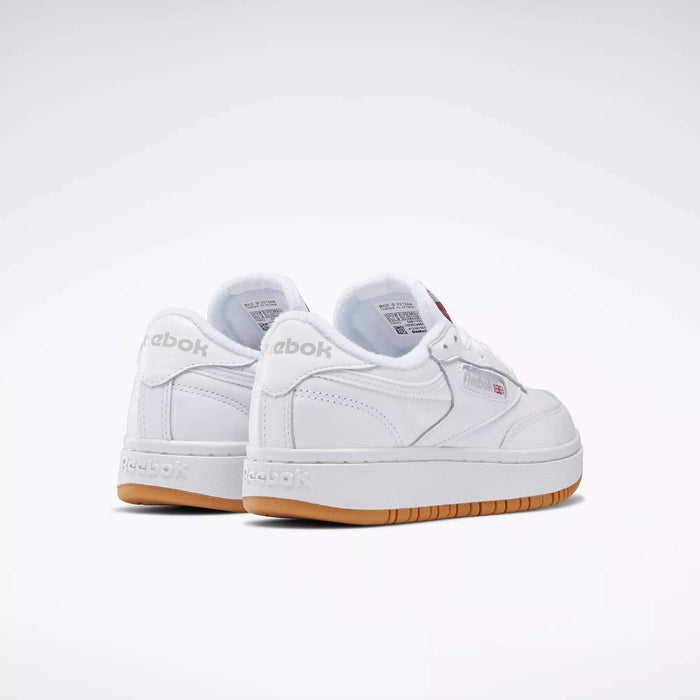 A pair of white Reebok Women's Club C Double Shoes with gum soles is shown from the back and side against a plain light background. The Reebok logo appears on both the heel and side of these classic tennis-inspired sneakers.