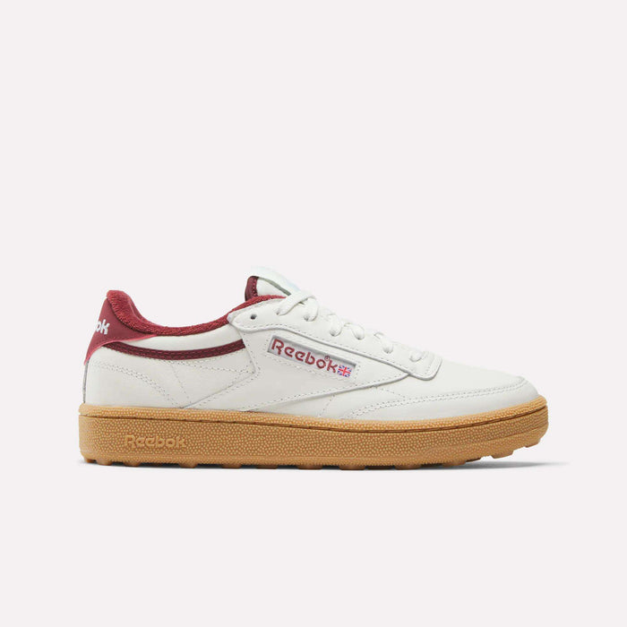 The Women's Club C Golf Shoes by Reebok are white sneakers with burgundy accents on the heel and tongue, a gum sole, spikeless outsole, and display the Reebok logo on the side.